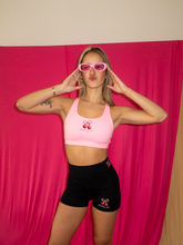 Load image into Gallery viewer, Light pink sports bra with a cherry bow design on the front and a strappy back, paired with black workout shorts with cherry bow design along the waistband