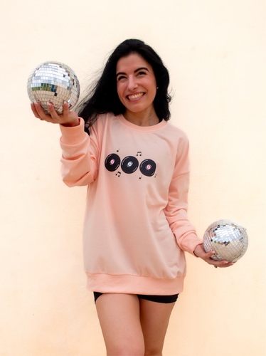 peach crewneck sweatshirt with 3 records that have music notes surrounding them printed on the front, and a colorful disco ball with the phrase 