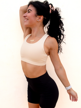 Load image into Gallery viewer, Young lady modeling a cream yellow colored sports bra with medium to high support and a unique racerback cut.