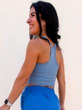 Load image into Gallery viewer, Young lady modeling a sky blue cropped racerback spandex tank with a built-in sports bra.