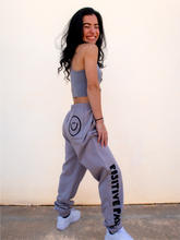 Load image into Gallery viewer, Peachy Pia Positive Pants joggers. Grey lightweight jogger sweatpants with positive pants design down the front of the right leg and smiley face design on the back pocket. Joggers provide an elastic waist and cuffed ankles.