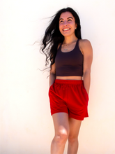 Load image into Gallery viewer, Young lady modeling comfortable red Sweatshorts in a lightweight material.