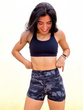 Load image into Gallery viewer, Young lady modeling Peachy Pia Peachy Shorts. Peachy Shorts are high-waisted in color black camo with a 75% nylon, 25% spandex blend. Extra stretchy fabric provides extra comfort while still providing a more fitted appearance.