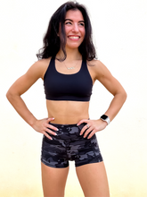 Load image into Gallery viewer, Young lady modeling Peachy Pia Peachy Shorts. Peachy Shorts are high-waisted in color black camo with a 75% nylon, 25% spandex blend. Extra stretchy fabric provides extra comfort while still providing a more fitted appearance.