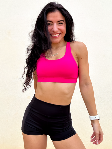 Young lady modeling Peachy Pia Worldwide Sports Bra. Sports bra is in color pink with an 87% nylon, 13% spandex blend. Material is thick but flexible made to provide support and comfort.