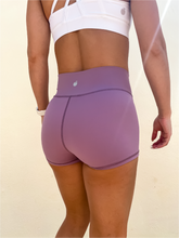 Load image into Gallery viewer, Young lady modeling Peachy Pia Peachy Shorts. Peachy Shorts are high-waisted in color lilac purple with a 75% nylon, 25% spandex blend. Extra stretchy fabric provides extra comfort while still providing a more fitted appearance.
