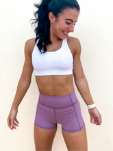 Load image into Gallery viewer, Young lady modeling Peachy Pia Peachy Shorts. Peachy Shorts are high-waisted in color lilac purple with a 75% nylon, 25% spandex blend. Extra stretchy fabric provides extra comfort while still providing a more fitted appearance.