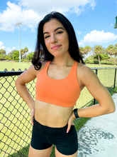 Load image into Gallery viewer, Young lady modeling Peachy Pia Worldwide Sports Bra. Sports bra is in color peach with an 87% nylon, 13% spandex blend. Material is thick but flexible made to provide support and comfort.