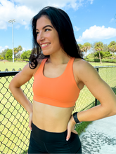 Load image into Gallery viewer, Young lady modeling Peachy Pia Worldwide Sports Bra. Sports bra is in color peach with an 87% nylon, 13% spandex blend. Material is thick but flexible made to provide support and comfort.
