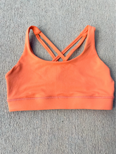Load image into Gallery viewer, Young lady modeling Peachy Pia Worldwide Sports Bra. Sports bra is in color peach with an 87% nylon, 13% spandex blend. Material is thick but flexible made to provide support and comfort.