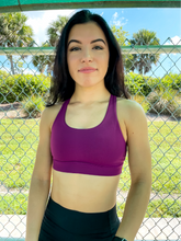Load image into Gallery viewer, Young lady modeling Peachy Pia Worldwide Sports Bra. Sports bra is in color purple with an 87% nylon, 13% spandex blend. Material is thick but flexible made to provide support and comfort.