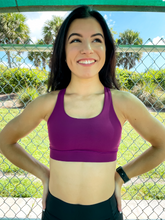 Load image into Gallery viewer, Young lady modeling Peachy Pia Worldwide Sports Bra. Sports bra is in color purple with an 87% nylon, 13% spandex blend. Material is thick but flexible made to provide support and comfort.