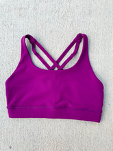 Load image into Gallery viewer, Young lady modeling Peachy Pia Worldwide Sports Bra. Sports bra is in color purple with an 87% nylon, 13% spandex blend. Material is thick but flexible made to provide support and comfort.