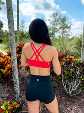 Load image into Gallery viewer, Young lady modeling Peachy Pia Worldwide Sports Bra. Sports bra is in color red with an 87% nylon, 13% spandex blend. Material is thick but flexible made to provide support and comfort.