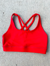 Load image into Gallery viewer, Young lady modeling Peachy Pia Worldwide Sports Bra. Sports bra is in color red with an 87% nylon, 13% spandex blend. Material is thick but flexible made to provide support and comfort.