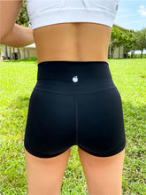 Load image into Gallery viewer, Young lady modeling Peachy Pia Peachy Shorts. Peachy Shorts are high-waisted in color black with a 75% nylon, 25% spandex blend. Extra stretchy fabric provides extra comfort while still providing a more fitted appearance.