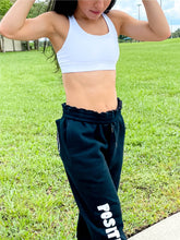 Load image into Gallery viewer, Young lady modeling Peachy Pia Positive Pants joggers. Black, fleece-lined joggers are made with a 100% cotton surface, coated in 100% polyester for increased durability with positive pants design down the front of the right leg and smiley face design on the back pocket. Joggers provide an elastic waist and cuffed ankles.