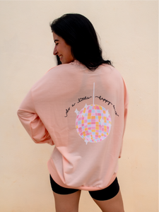 peach crewneck sweatshirt with 3 records that have music notes surrounding them printed on the front, and a colorful disco ball with the phrase "do a little happy dance" printed on the back