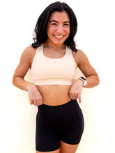 Load image into Gallery viewer, Young lady modeling a cream yellow colored sports bra with medium to high support and a unique racerback cut.
