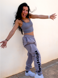 Peachy Pia Positive Pants joggers. Grey lightweight jogger sweatpants with positive pants design down the front of the right leg and smiley face design on the back pocket. Joggers provide an elastic waist and cuffed ankles.