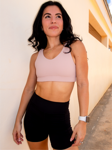 Young lady modeling a ribbed, beige sports bra that has medium/high support with a v neck front and scoop neck back.