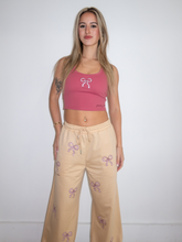 Load image into Gallery viewer, Pink cropped tank top with a built-in sports bra and bow design on the front paired with tan sweatpants with pink bow pattern
