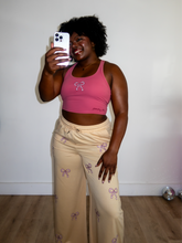 Load image into Gallery viewer, Pink cropped tank top with a built-in sports bra and bow design on the front paired with tan sweatpants with pink bow pattern
