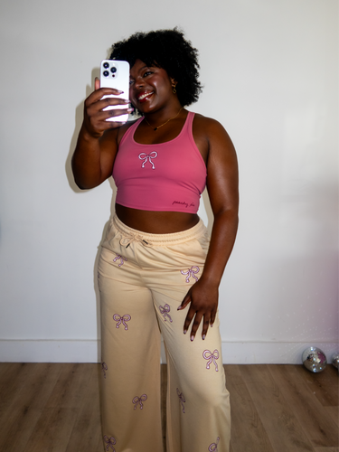 Pink cropped tank top with a built-in sports bra and bow design on the front paired with tan sweatpants with pink bow pattern