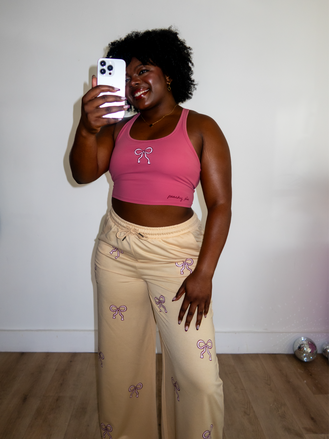 Pink cropped tank top with a built-in sports bra and bow design on the front paired with tan sweatpants with pink bow pattern