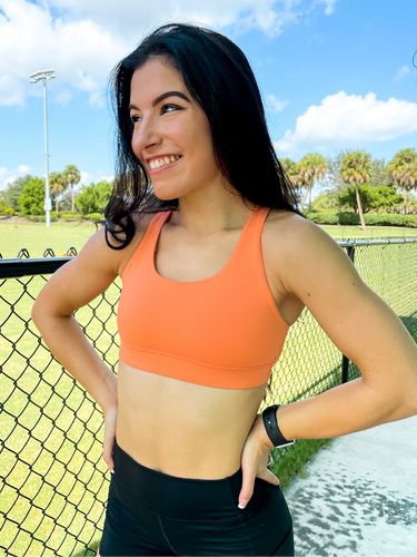 Young lady modeling Peachy Pia Worldwide Sports Bra. Sports bra is in color peach with an 87% nylon, 13% spandex blend. Material is thick but flexible made to provide support and comfort.