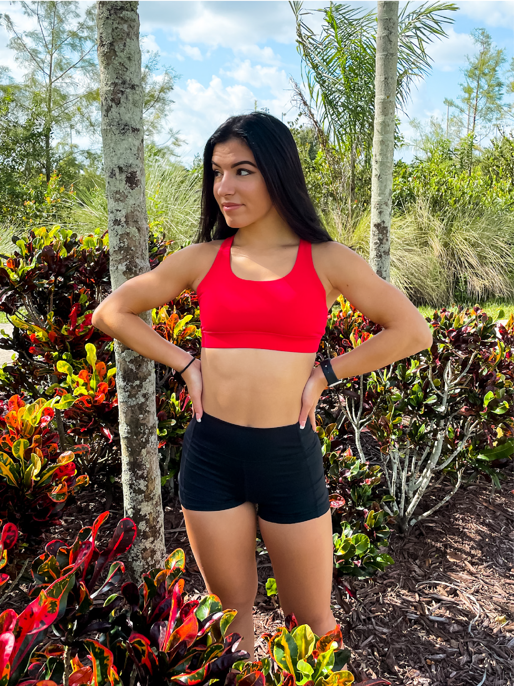 Young lady modeling Peachy Pia Worldwide Sports Bra. Sports bra is in color red with an 87% nylon, 13% spandex blend. Material is thick but flexible made to provide support and comfort.