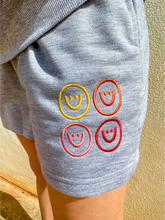 Load image into Gallery viewer, Grey, lightweight sweatshorts with multicolored smiley faces embroidered.
