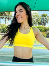 Load image into Gallery viewer, Young lady modeling Peachy Pia Worldwide Sports Bra. Sports bra is in color yellow with an 87% nylon, 13% spandex blend. Material is thick but flexible made to provide support and comfort.
