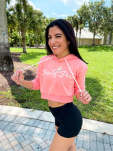 Load image into Gallery viewer, Young lady modeling Peachy Pia cropped hoodie. Cropped hoodie is Terry material with a 70% cotton, 30% polyester blend in a pinkish-peach color and has the official Peachy Pia logo on the front.
